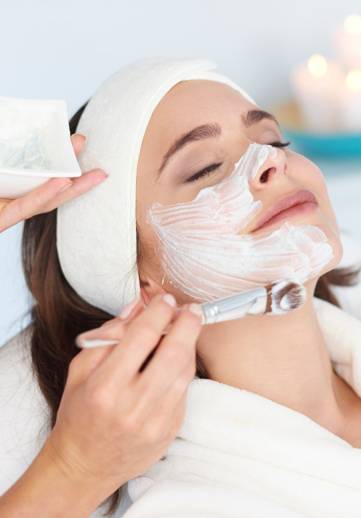 a woman who is laying and a doctor is applying skin care cream on her face